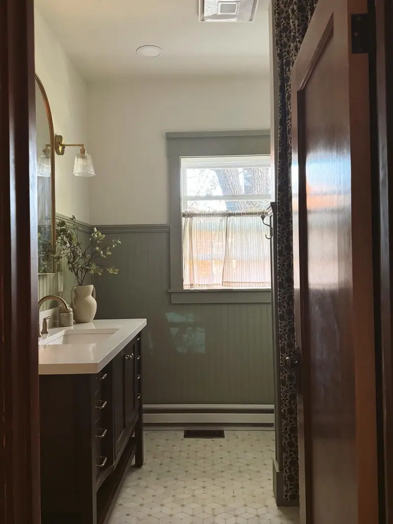 Bathroom remodel in Salisbury, MO, after: sage beadboard, brass sconces, and a dark wood vanity